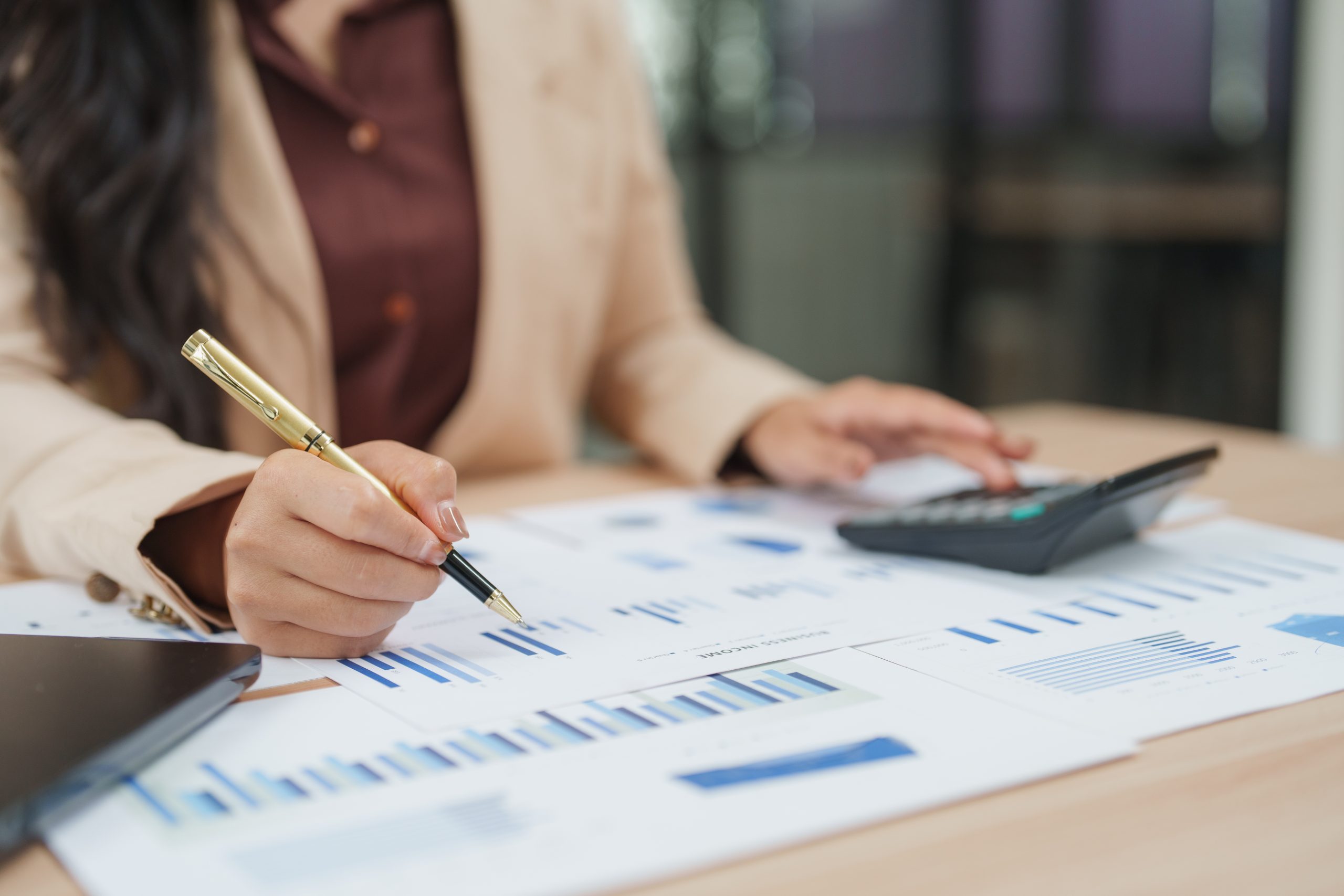 Businesswoman analyzing financial charts and using calculator in office
